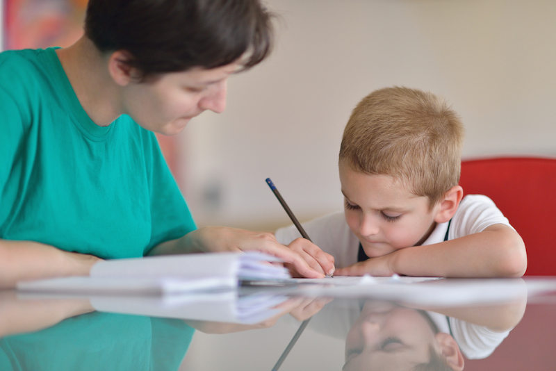 Woman helping boy with homework at a table